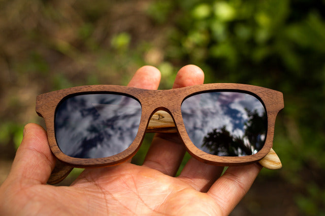 mano sosteniendo Lentes wirrarika de madera shabby, marca bang, fondo de naturaleza